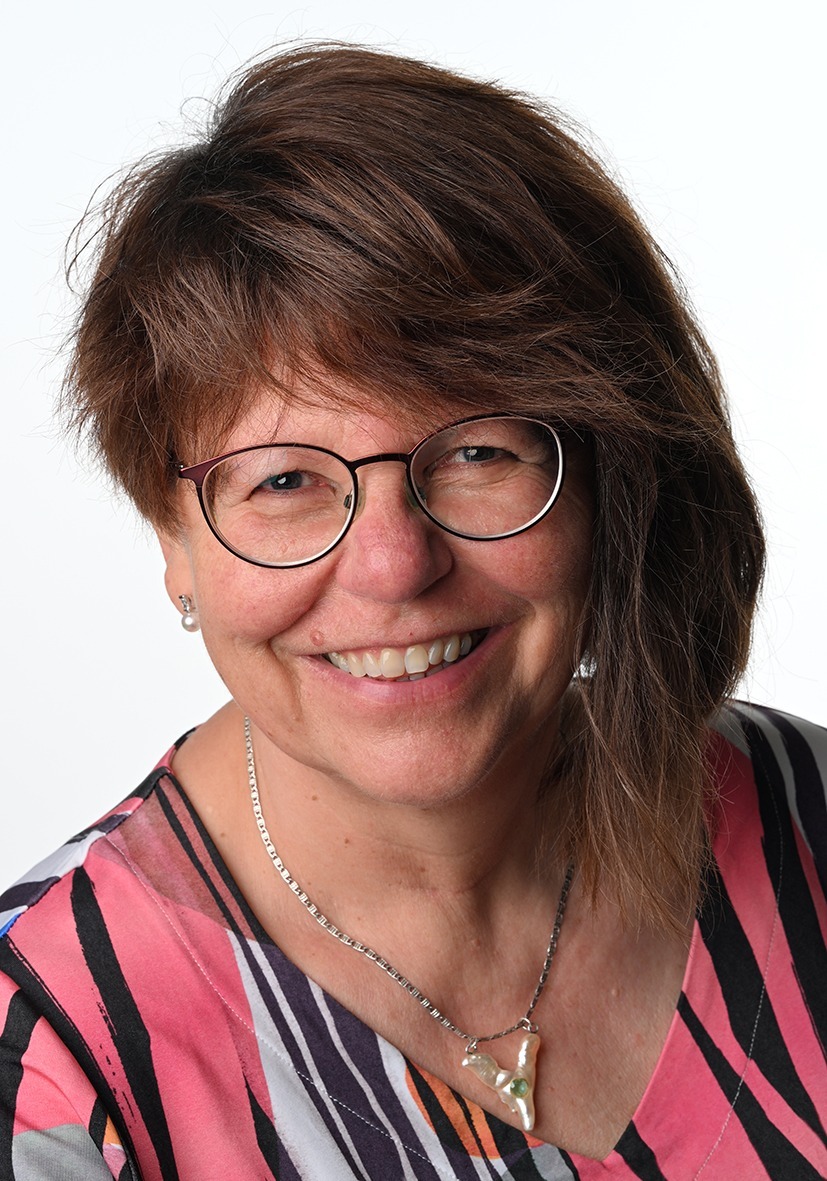 Frau mit schulterlangem braunem Haar, trägt eine silberne Kette und ein bunt gestreiftes Oberteil in Pink, Schwarz und Weiß