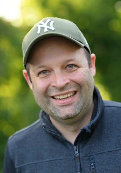 Person trägt eine olivgrüne Baseballkappe mit weißem New York Yankees Logo und eine dunkelblaue Jacke mit Reißverschluss